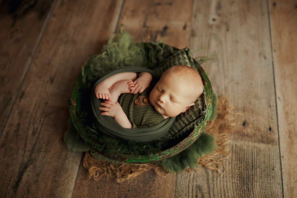 Baby boy swaddled in earth tones and lying in wooden bowl prop