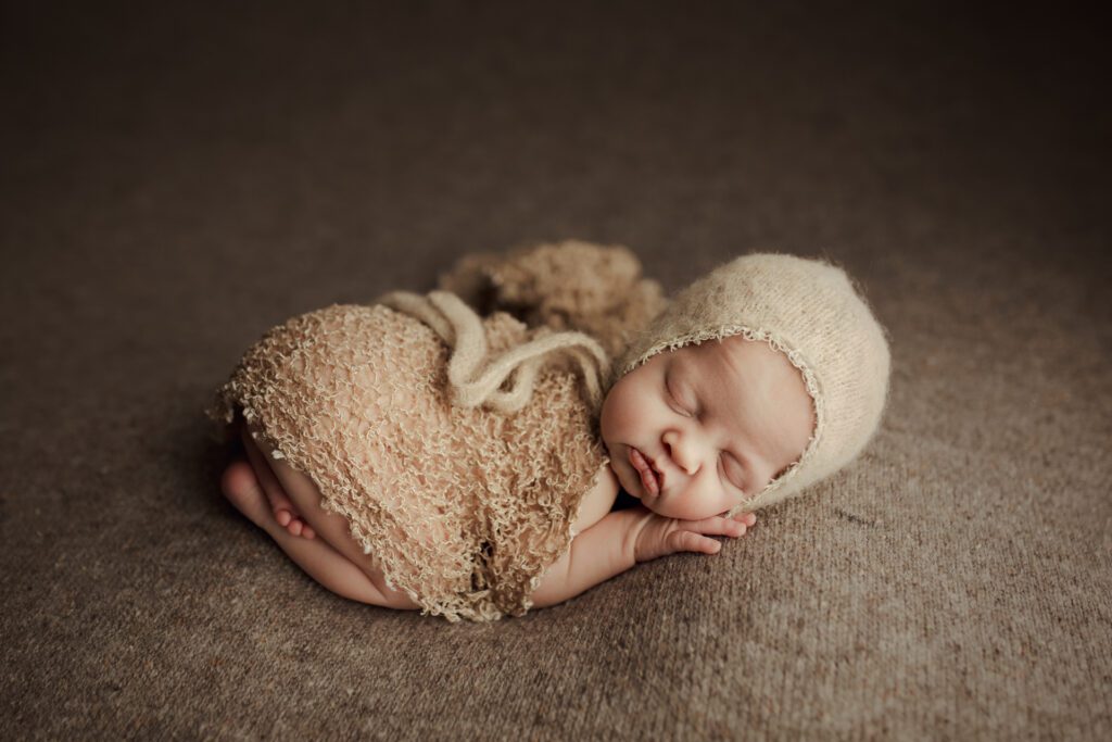 Sleeping baby girl in cap and light brown blanket in Chicago suburbs studio