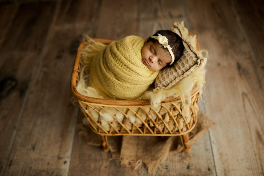 Sleeping infant girl in yellow swaddle cradled atop pillows