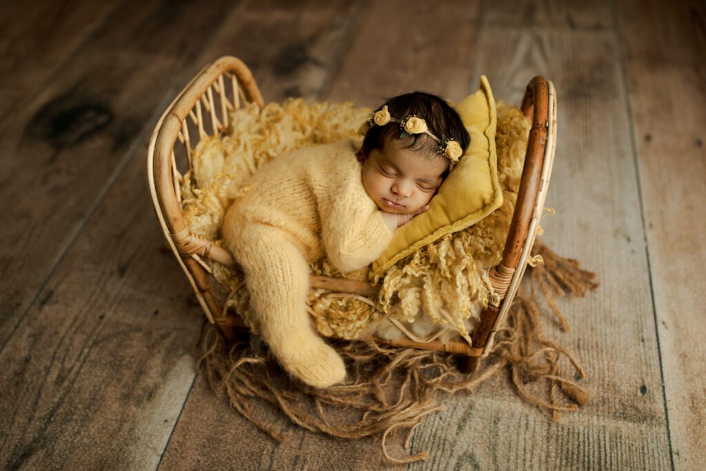 Baby girl in yellow footies asleep on miniature crib