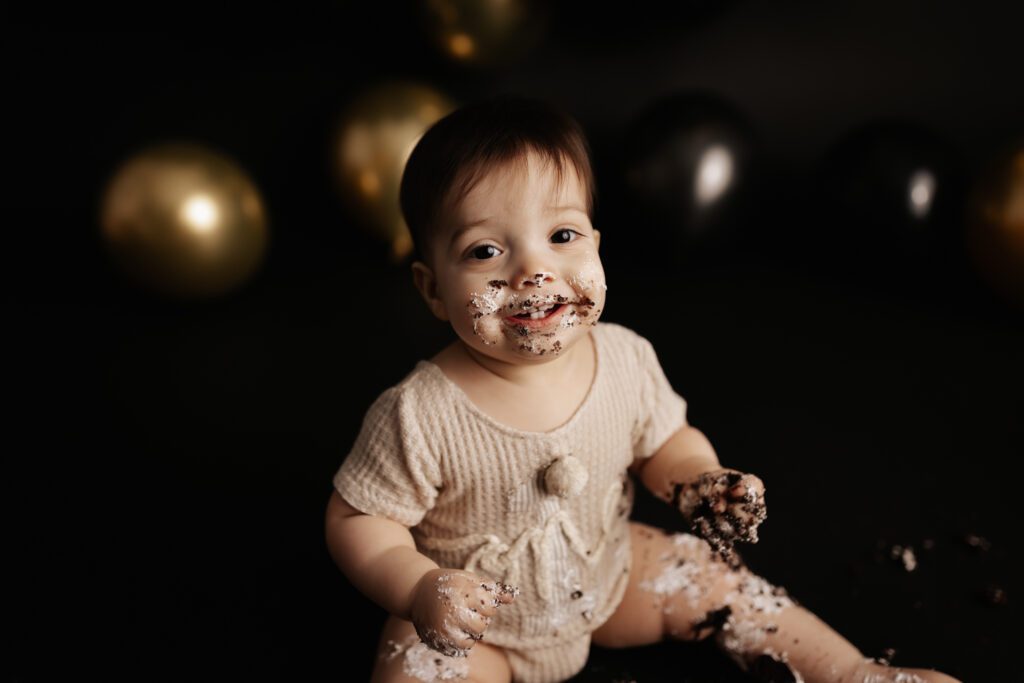 Baby boy covered in cake and smiling during first birthday cake smash session near Highland Park