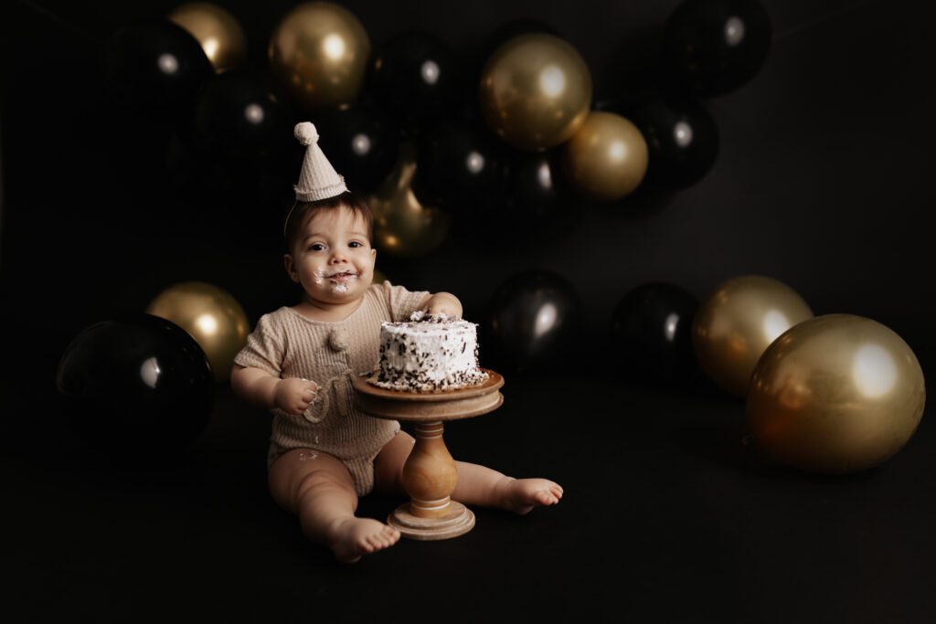 One-year-old boy in birthday hat digging into his cake at photo studio near Highland Park, Illinois