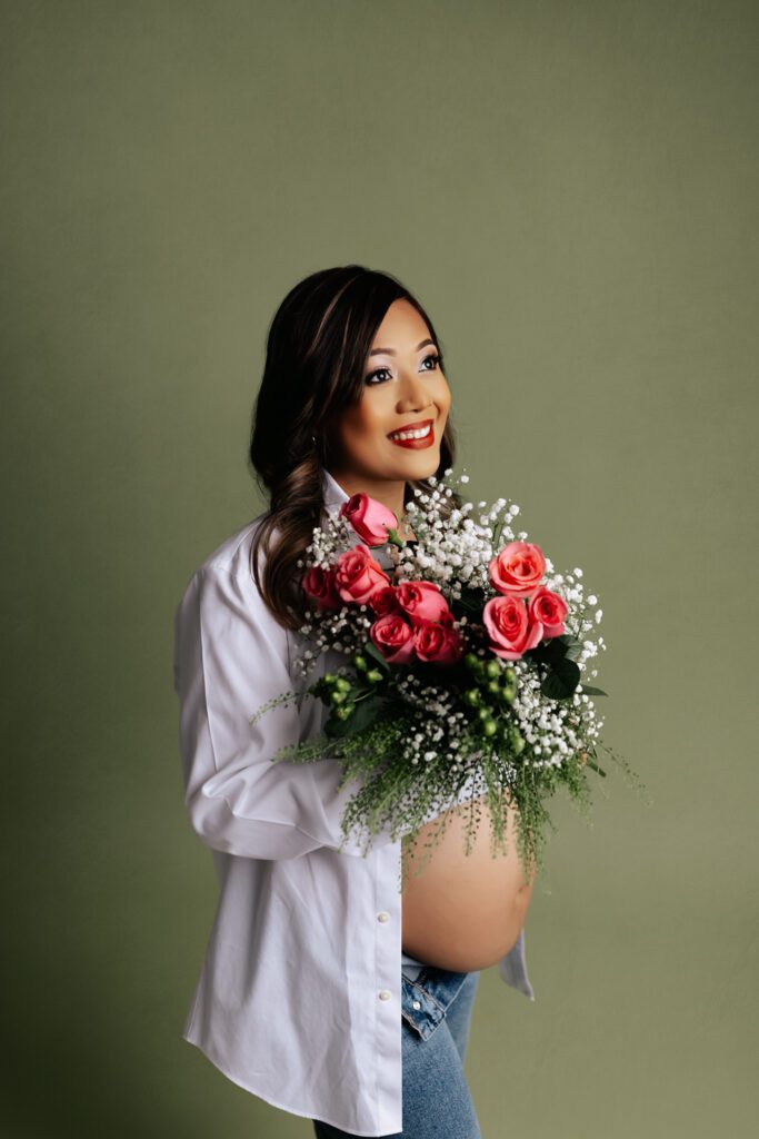 Pregnant woman in jeans and unbuttoned white blouse holding a bouquet of roses