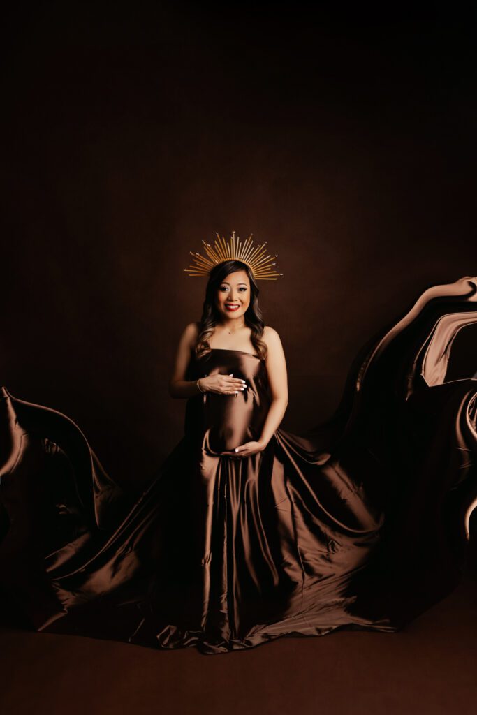 Asian woman in silk maternity wrap with gold sunray crown perched on her head