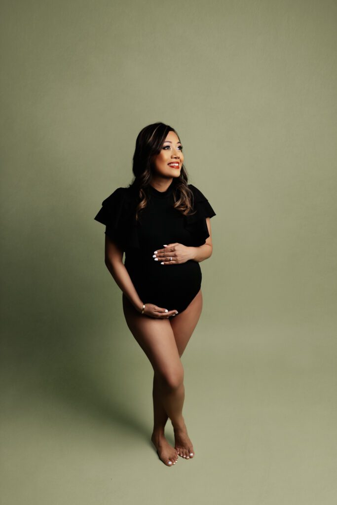 Asian woman in ruffled black bodysuit poses for maternity photos in Chicago studio