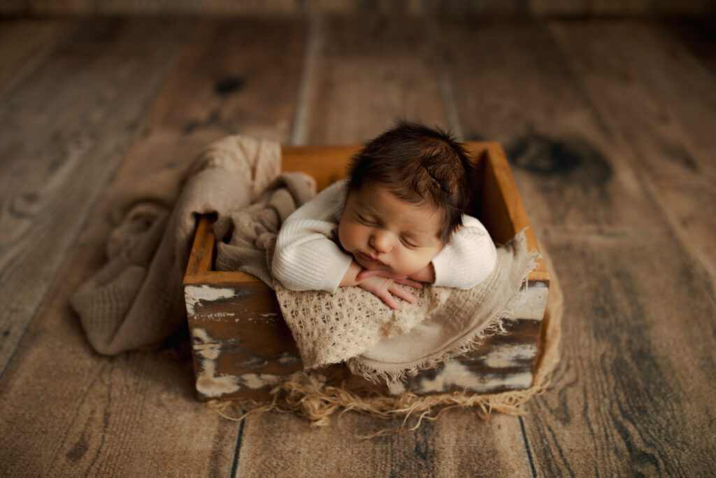 Baby boy asleep in distressed wooden box cushioned with blankets