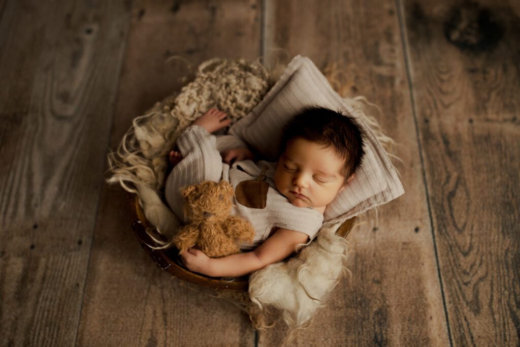 Infant boy curled up asleep with his teddy bear by his side