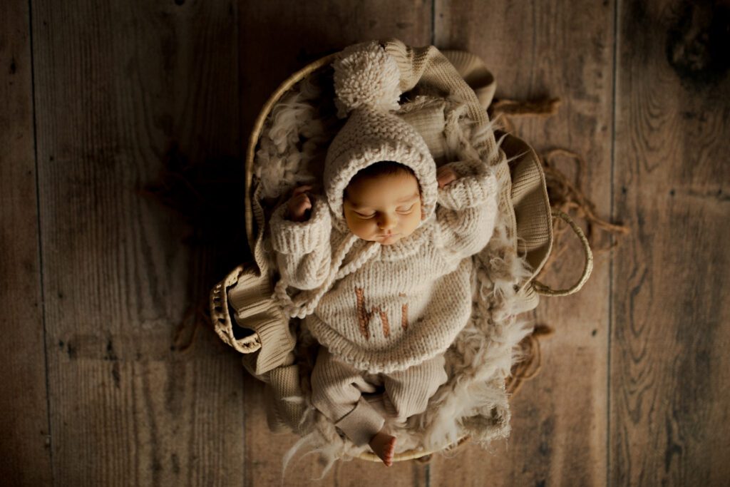 baby boy in cozy sweater and bobble hat asleep in basket in Chicago studio