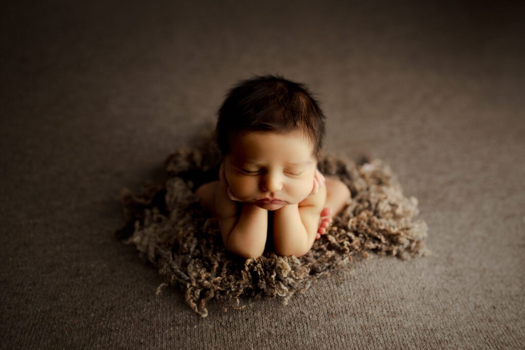 Newborn boy asleep in froggy pose on a comfy yarn rug
