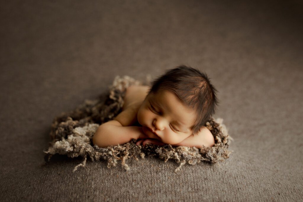 Newborn boy with dark hair asleep on comfy textured beanbag