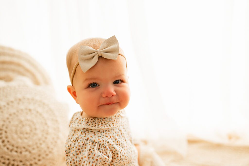 Baby girl in old-fashioned print dress and bow smiles during her sitter session in Chicago