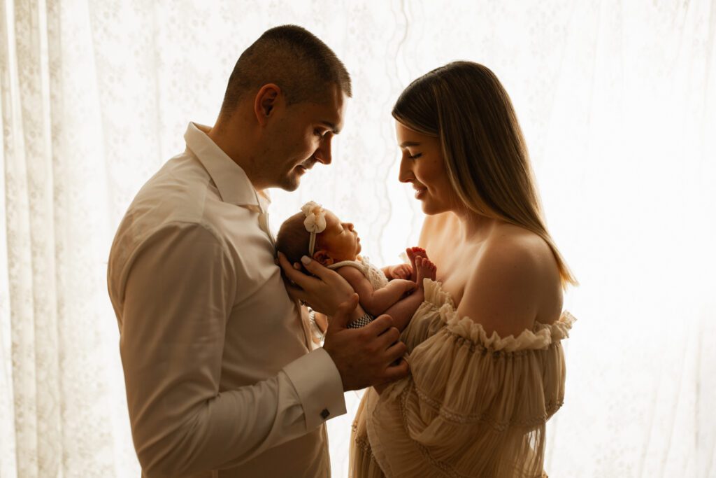 Chicago parents hold their new baby daughter, backlist against a window