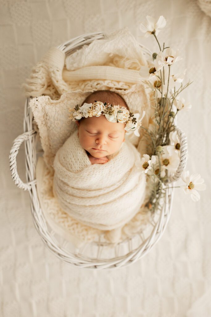 Baby girl in white swaddle and flower crown nestled in a basket in photo studio near Chicago Illinois