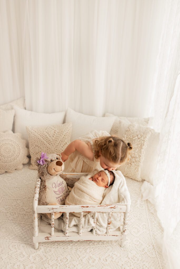 Toddler girl leans over crib to kiss her new baby sister 