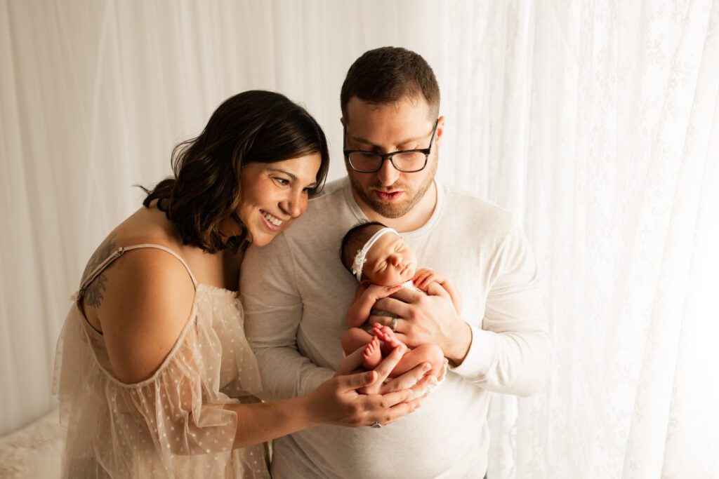 Dad holds new baby girl up to his chest while mom leans against his shoulder 