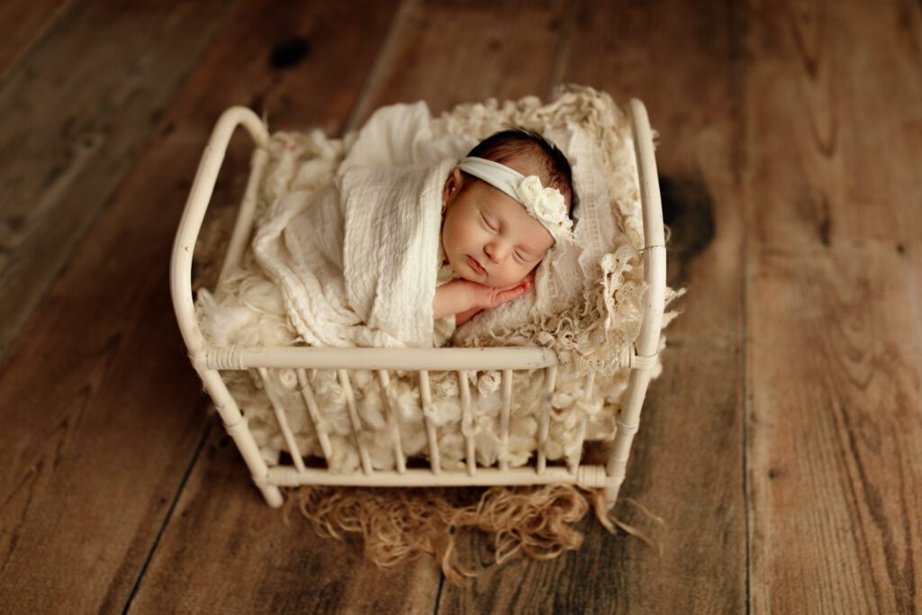 Infant girl tucked cozily into a miniature crib during her newborn photo session in Chicago Illinois