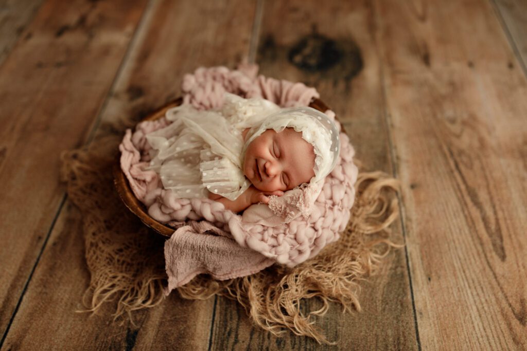 Smiling baby curled up in a wooden bowl prop with lots of textured blankets