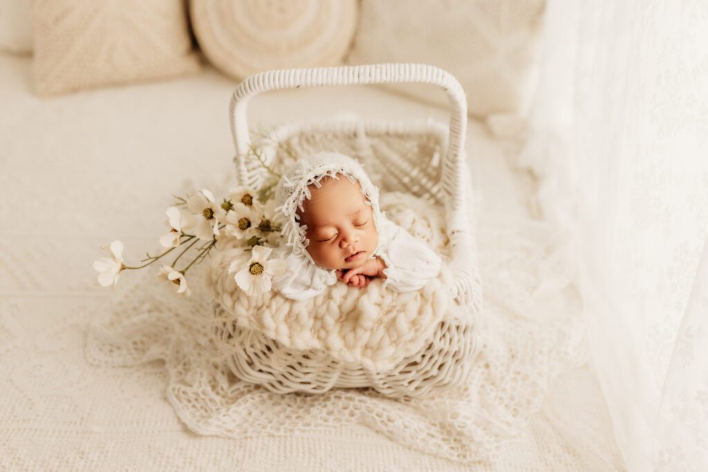 Baby asleep in white wicker basket with a sprig of flowers tucked in next to her