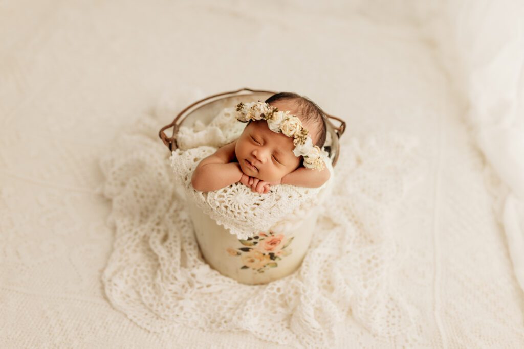 Newborn girl wearing flower wreath asleep in shabby chic bucket in Chicago portrait studio