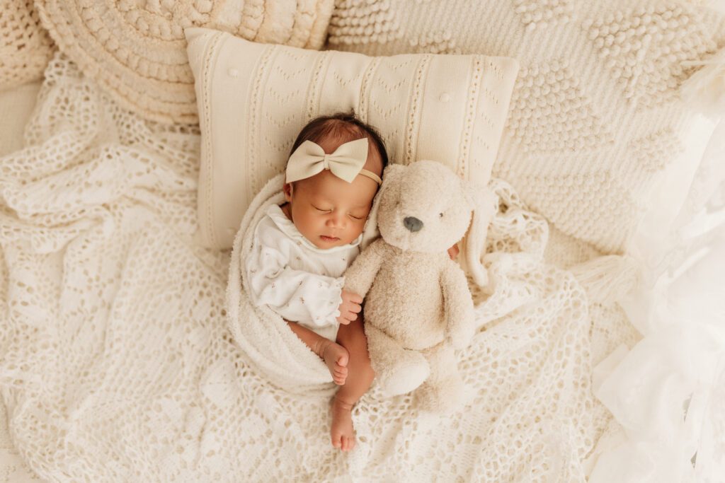 Newborn baby girl in blanket and bow snuggling a white teddy