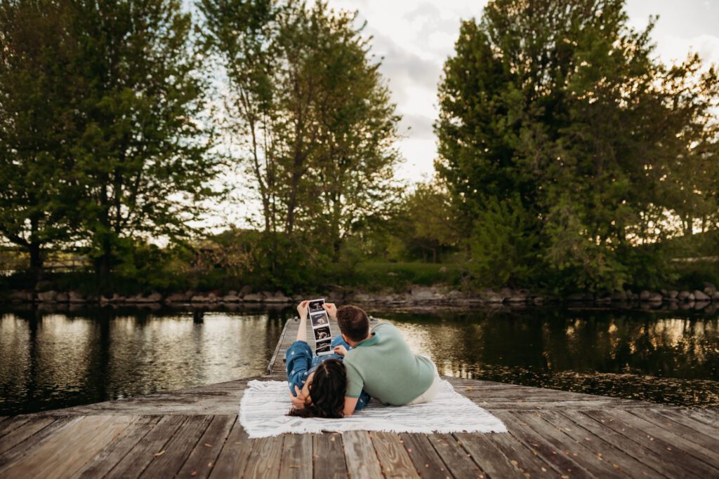 Couple lying on a blanket by the lake looking at ultrasound images of their baby