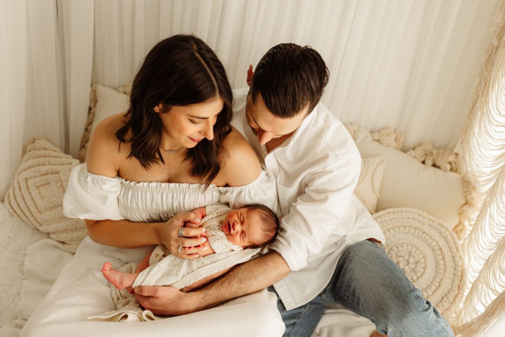 New parents seated in cozy, curtained nook holding their new baby boy