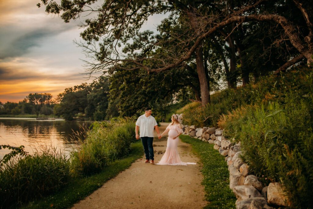 Couple walking on path by Chicagoland lake at sunset and holding hands