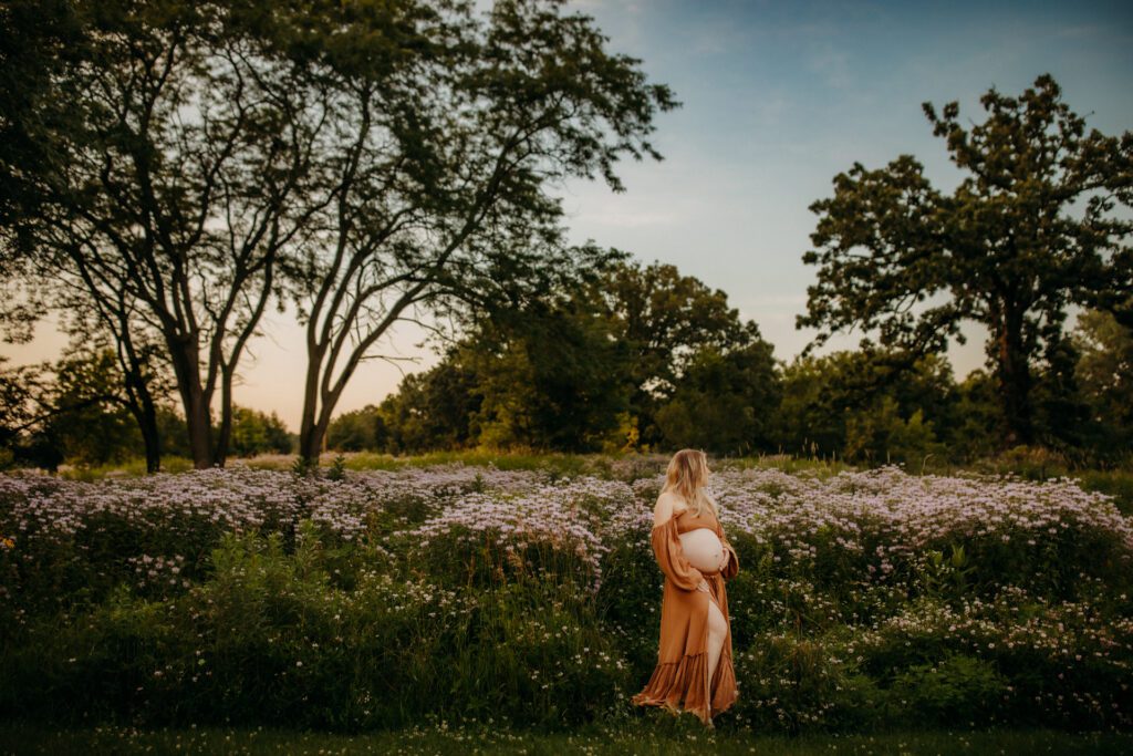 Pregnant woman gazes into the distance across a field of wildflowers