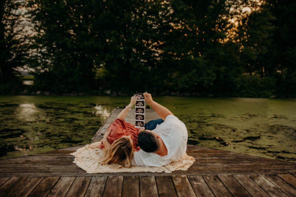 Couple lying on wooden dock looking at sonogram of their baby