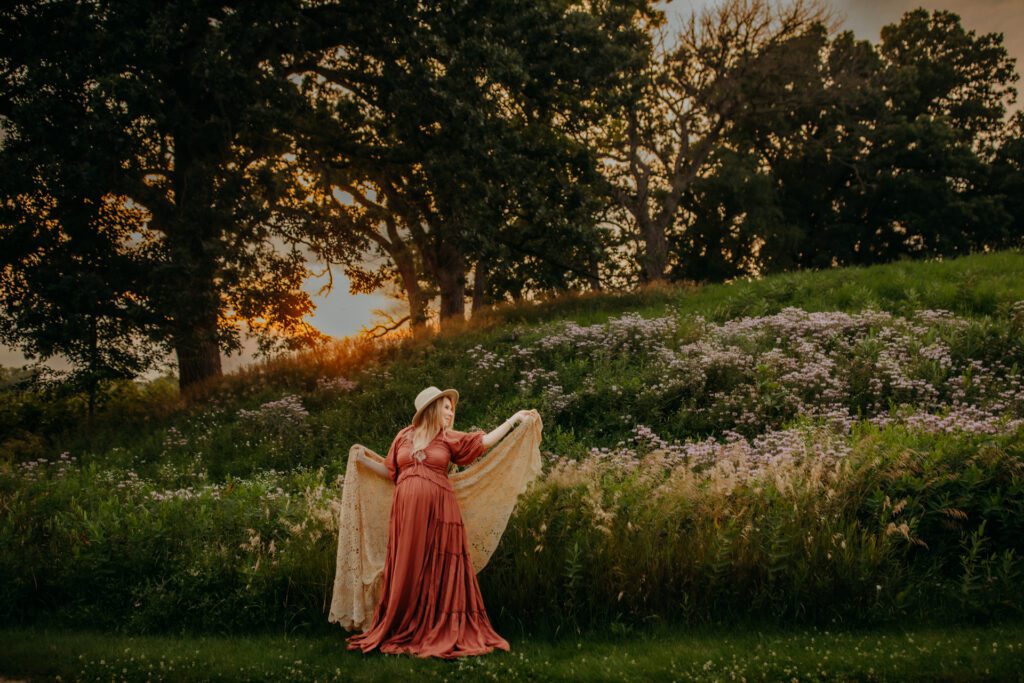 Pregnant woman in boho maternity dress wraps a lacy shawl around herself during her sunset maternity shoot