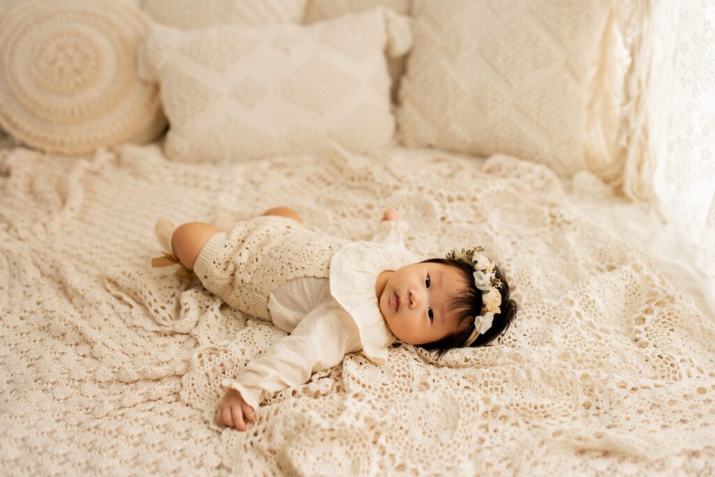 Cute baby girl with black hair and flower crown reclining on a bed setup in Long Grove Illinois studio near Chicago