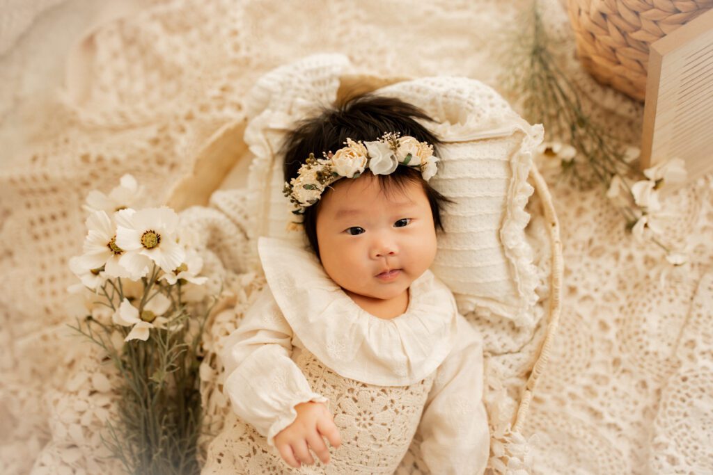 Asian-American baby girl smiling next to a bouquet of wildflowers during her 100 days milestone photoshoot