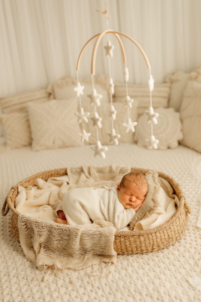 Baby boy curled up asleep in a shallow wicker basket with a star mobile above him