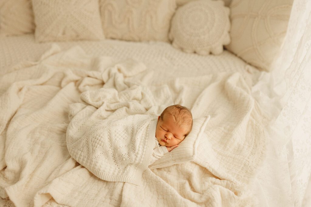 New baby boy asleep on a pillow and bundled snugly in blankets during a newborn photoshoot near Chicago