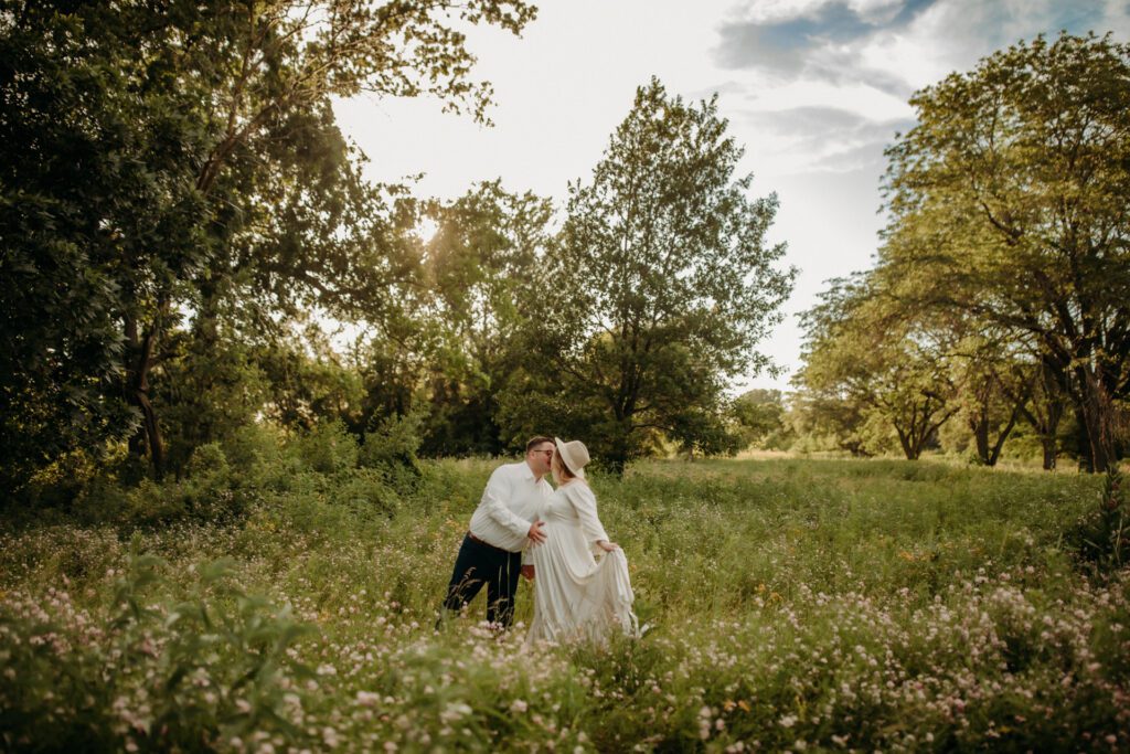 Couple exchange a kiss in a secluded Illinois meadow during their maternity photoshoot