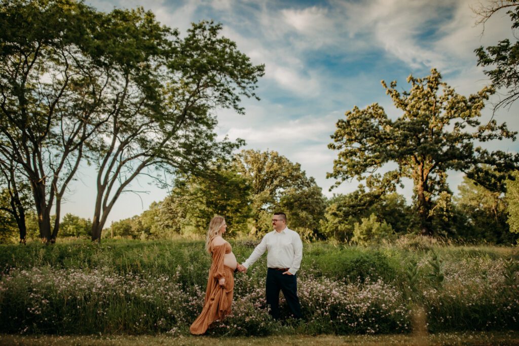 Man and woman hold hands in a wildflower meadow near Chicago during a maternity photo session