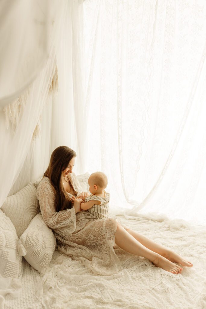 Mom leans back against pillows in a pretty lifestyle setup as she plays with her baby