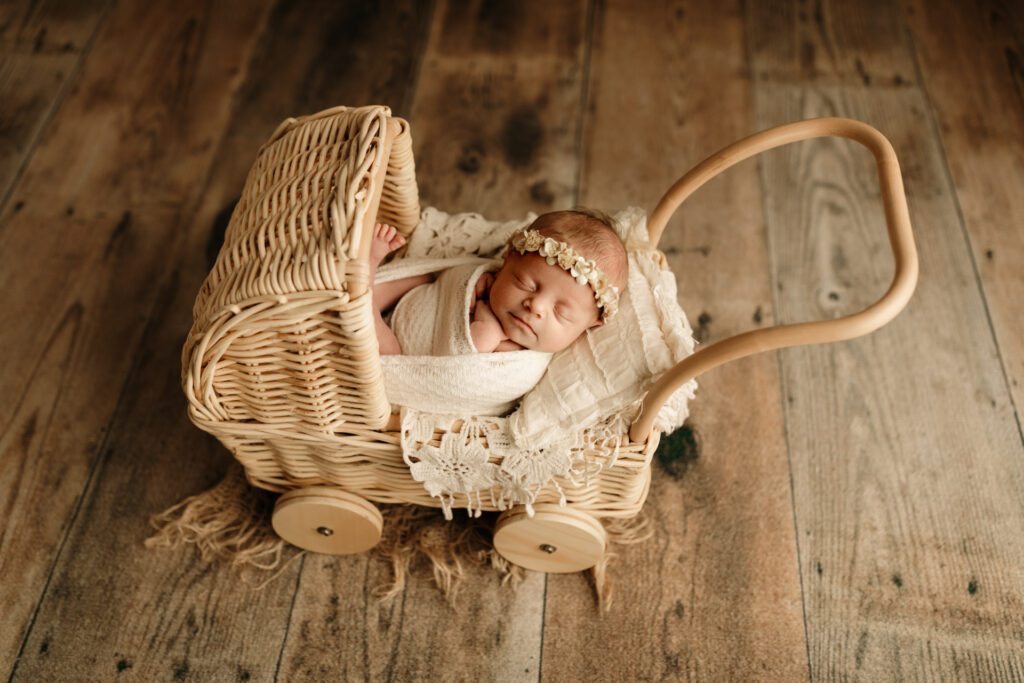 Baby girl wearing flower crown and sleeping in a tiny wicker stroller with wooden wheels