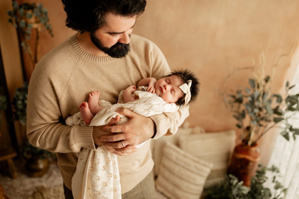 Dad holds his newborn daughter in his arms in a warmly lit studio space near his home in Vernon Hills, IL