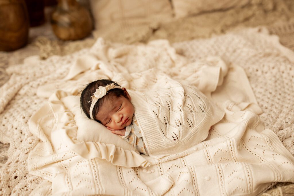 Infant girl asleep on a pile of white blankets during her lifestyle studio newborn photography session