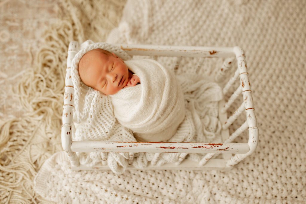 Swaddled baby boy sleeps in antique white crib during his newborn photography session in Chicago's northwest suburbs