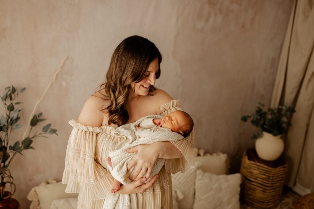 Mother in cream-colored boho dress smiles down at her newborn baby during a lifestyle studio photoshoot in Chicago