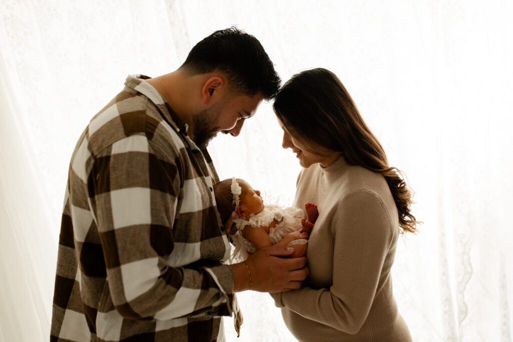 Parents lean into each other as they hold their newborn daughter between them during a Chicago photoshoot