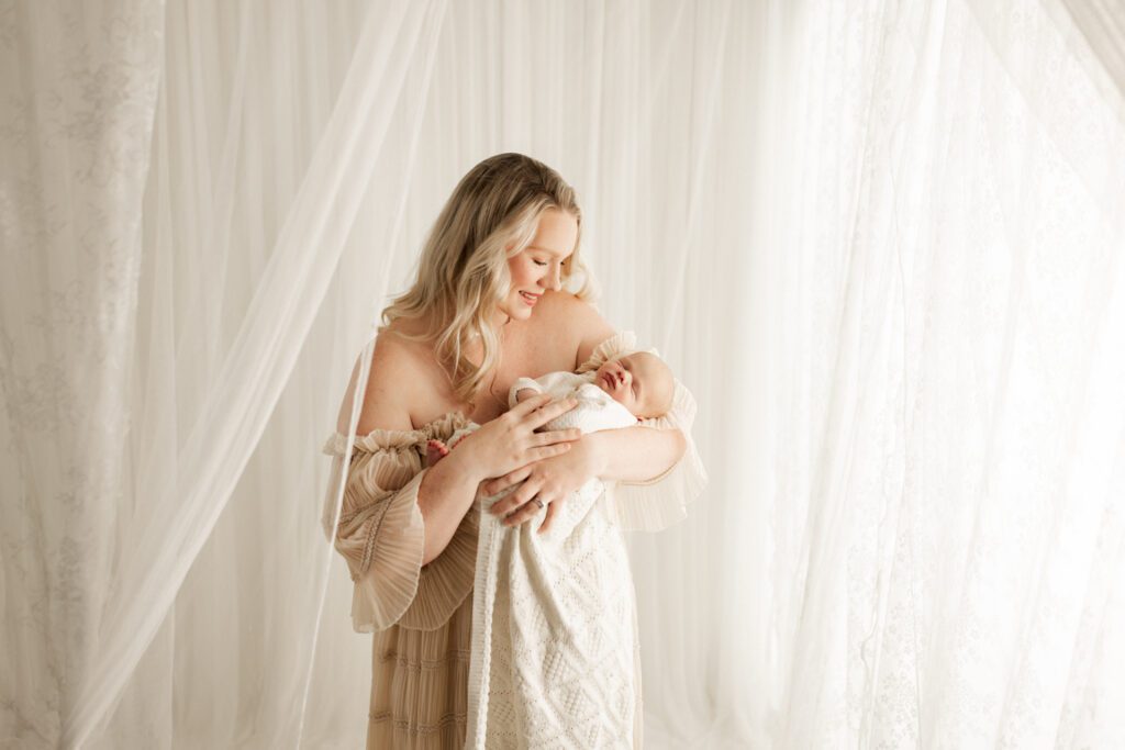 Mother in boho dress holds her new baby boy close during a newborn session in Chicago area studio