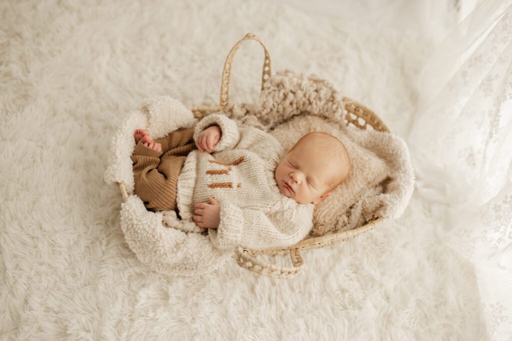 Baby boy in chunky sweater asleep in basket with cozy blankets