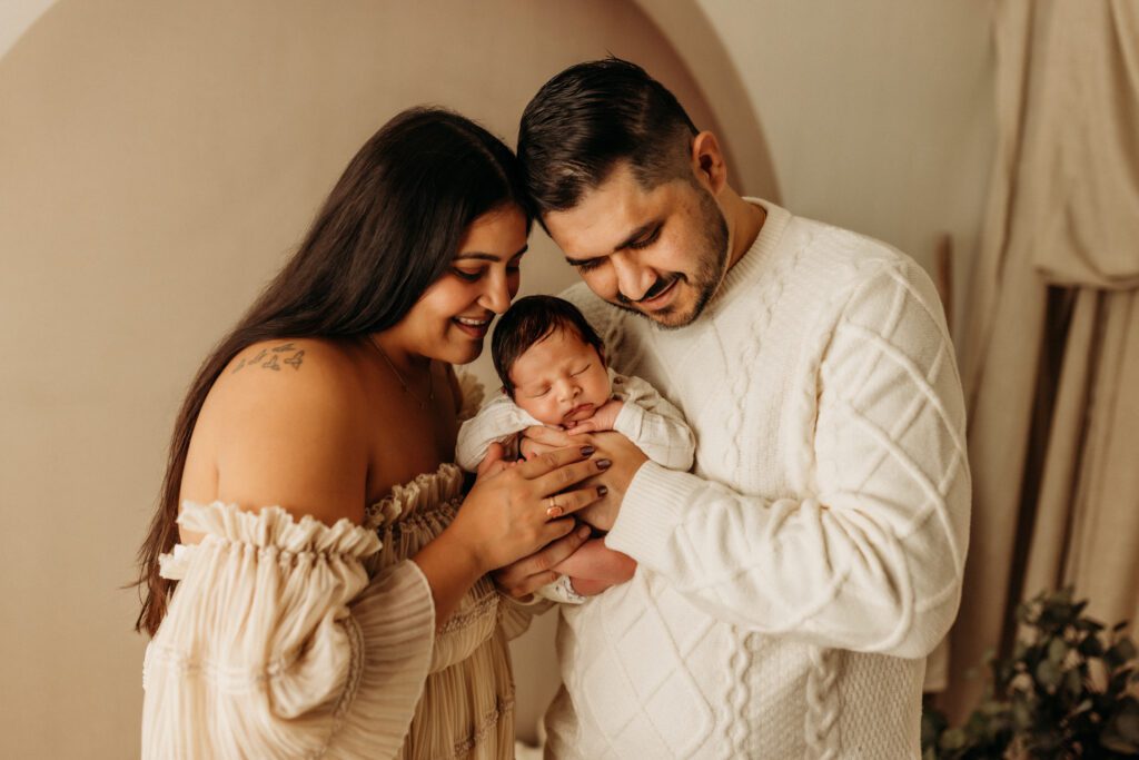 New parents lean into each other as they hold their baby between them in a lifestyle studio near their home in Huntley Illinois