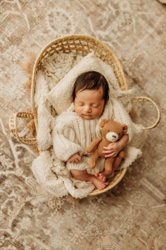 Baby boy in a soft knitted sweater sleeps peacefully in a basket with a tiny bear tucked under his arm