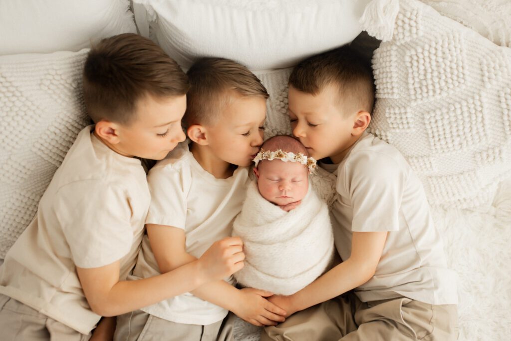 Three young boys lying together on a bed with their swaddled baby sister snuggled between them