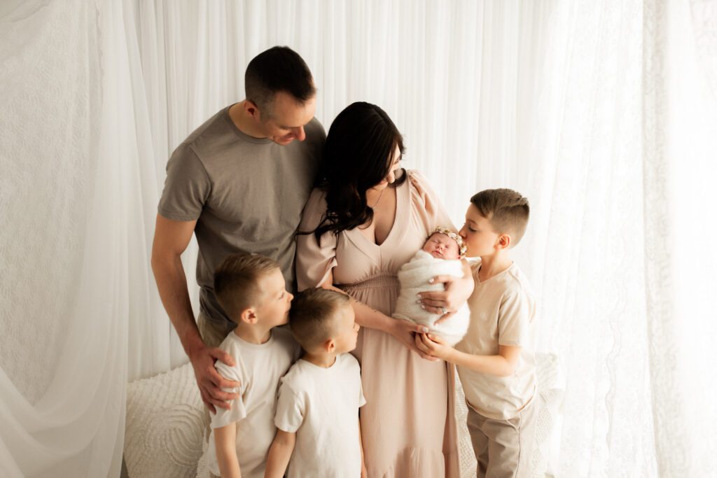 Family gathers around Mom as she holds baby in her arms while big brother kisses the top of baby's head