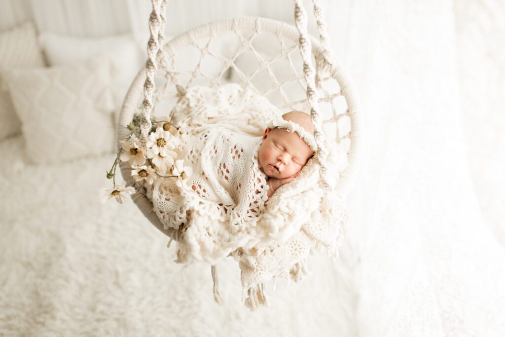 Sleeping infant in a white macrame swing with a sprig of daisies beside her